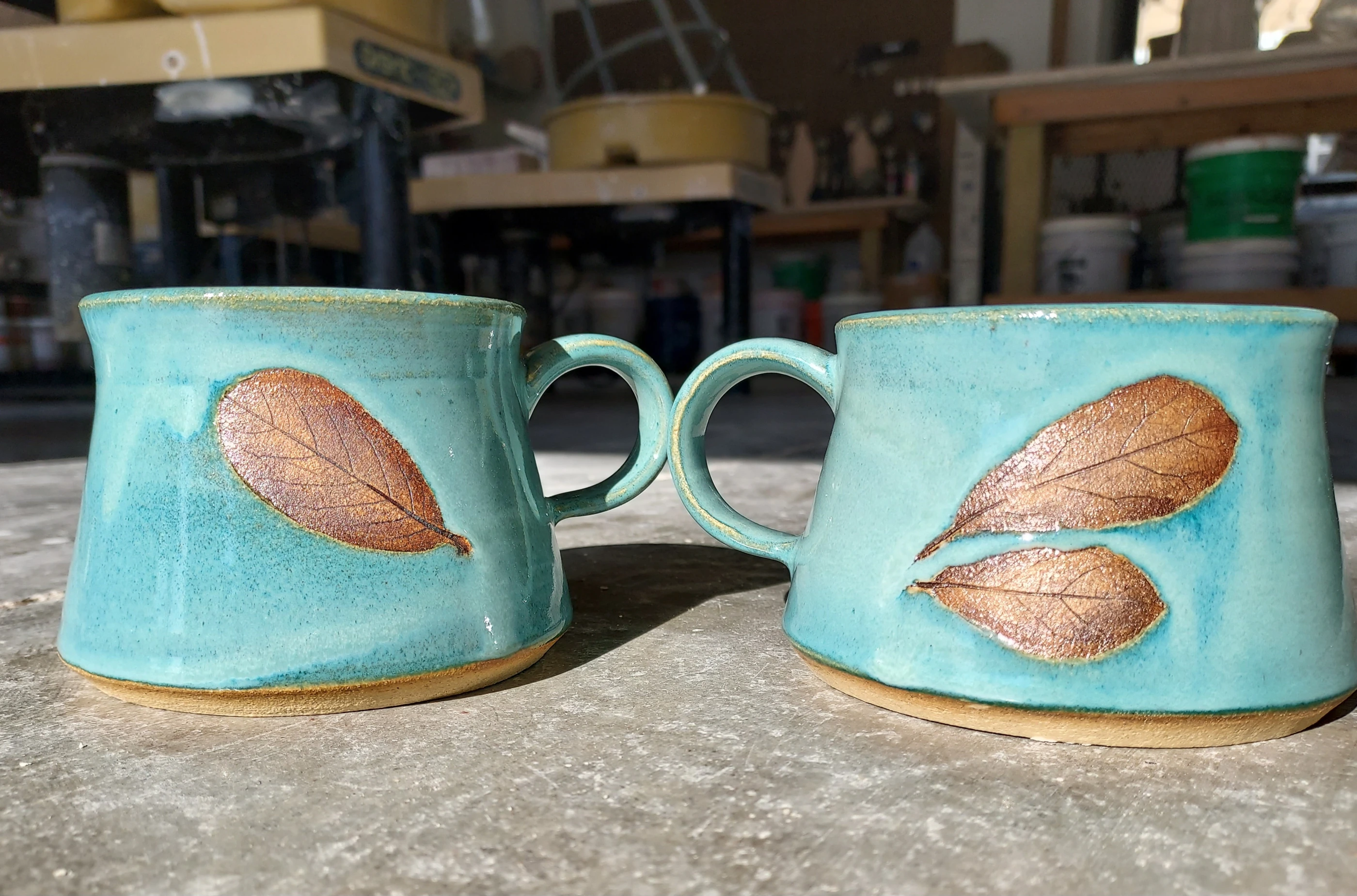 Close view of the copper-brown leaf impressions and turquoise glaze on the original mugs