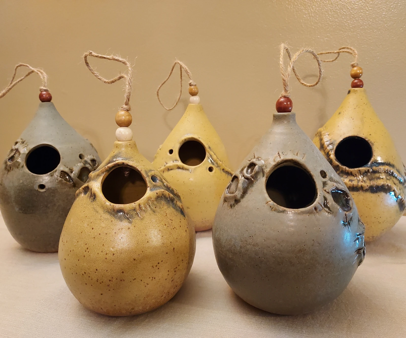 Five earthy grey and yellow hanging ceramic bird forms, photographed with their original backdrop